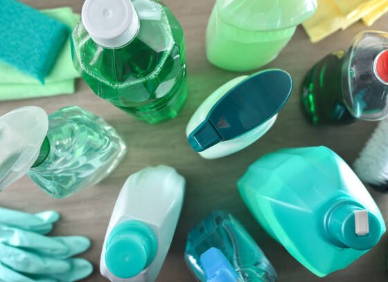 Supply of general cleaning products with several disinfectant bottles and tools such as rags, scouring pads, gloves and brushes on wooden table. Top view.